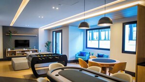 A modern living room with a foosball table, comfortable seating, a flat-screen TV, and large windows. - Parking Space, View, and Complete Amenities in the City Center | LYVVO (Campinas)