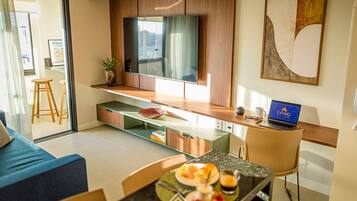 Uma sala de estar moderna com televisão, laptop e um espaço de jantar com mesa e cadeiras de vidro.