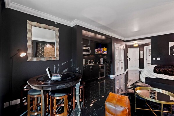 Una habitación de hotel moderna con una paleta de colores blanco y negro, una mesa de comedor redonda, un sofá, una cama y una zona de cocina.