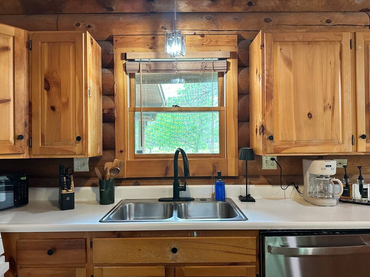 A wooden cabin kitchen with a double sink, wooden cabinets, a window, and a coffee maker.