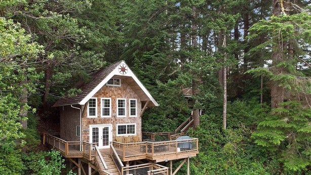 A wooden house with a deck, surrounded by trees.