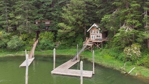 A wooden house on stilts over water, surrounded by dense forest.