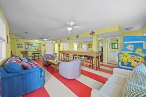 A brightly colored living room with a red and white striped rug, a blue sofa, a white sofa, and a dining area with a wooden table and chairs. - Luxury Waterfront & Oceanfront Beach Paradise (North Topsail Beach)