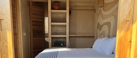 A bedroom with a bed, a shelf unit, and a wall-mounted air conditioner.