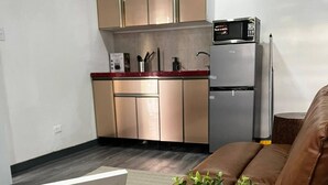 Un espacio habitable compacto con kitchenette, un televisor de pantalla plana sobre una mesa de madera y una cesta tejida con plantas verdes.