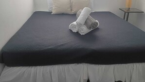 Una cama bien hecha con una colcha oscura, dos almohadas y toallas enrolladas sobre la cama.