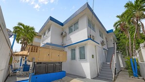 Un edificio di due piani con una scalinata che conduce al piano superiore, una combinazione di colori blu e bianco e una palma sullo sfondo.
