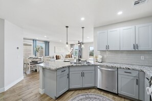 Une cuisine moderne avec des meubles gris, un plan de travail en granit et des luminaires suspendus.