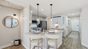Une cuisine moderne dotée d’un îlot central, d’un éclairage suspendu et donnant sur l’espace de vie adjacent.