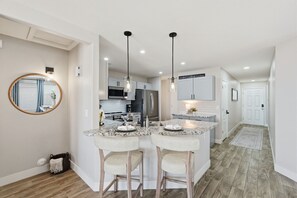 Une cuisine moderne dotée d’un îlot central, d’un éclairage suspendu et donnant sur l’espace de vie adjacent.