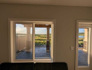 A room with a large sliding glass door leading to an outdoor patio with a stone column and a view of a lake. - 2 Bedroom Suite (Contact for Short-stay) (Calgary)