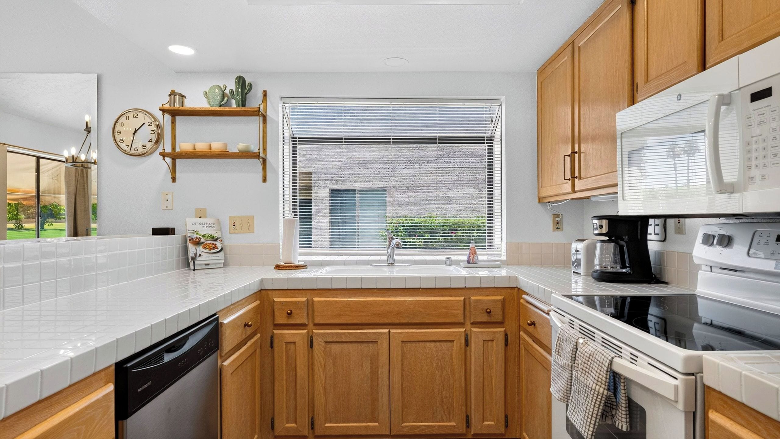 A kitchen with wooden cabinets, a white countertop, a built-in oven, a microwave, and a window with blinds.