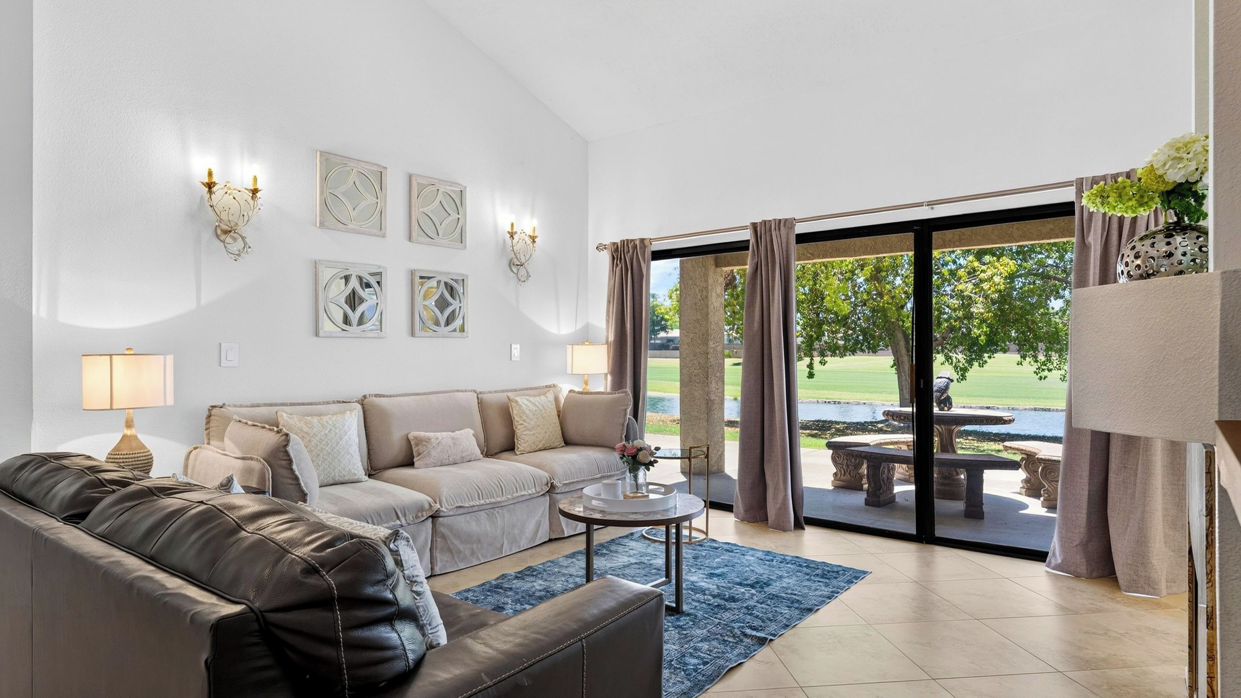 Un salon moderne avec un canapé en cuir, une table basse et une vue sur un jardin, visible à travers de grandes portes vitrées.