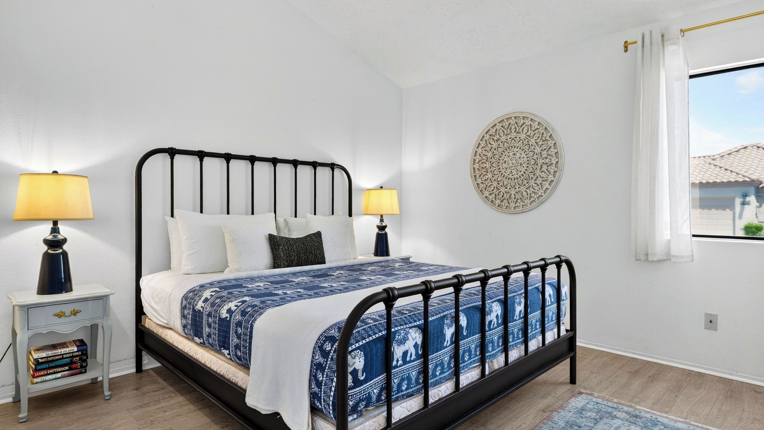 A neatly arranged bedroom with a bed, bedside tables, a wall decoration, and a window with curtains.