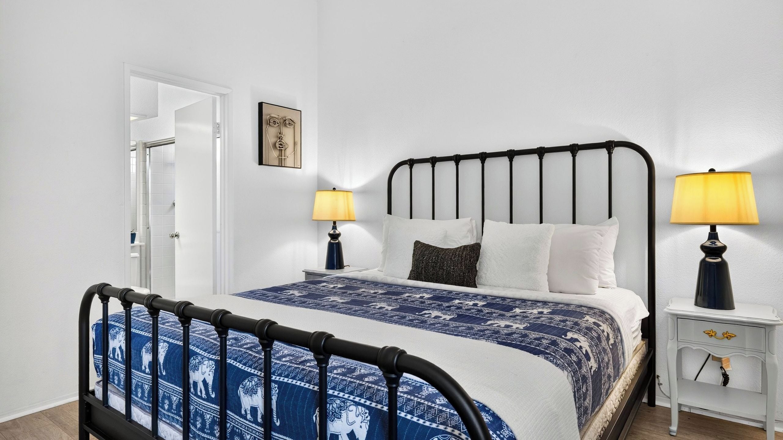 Une chambre à coucher avec un lit, deux tables de chevet, une porte et un tableau accroché au mur.