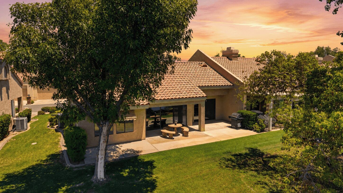 A residential house with a patio, a large tree, and a clear sky.