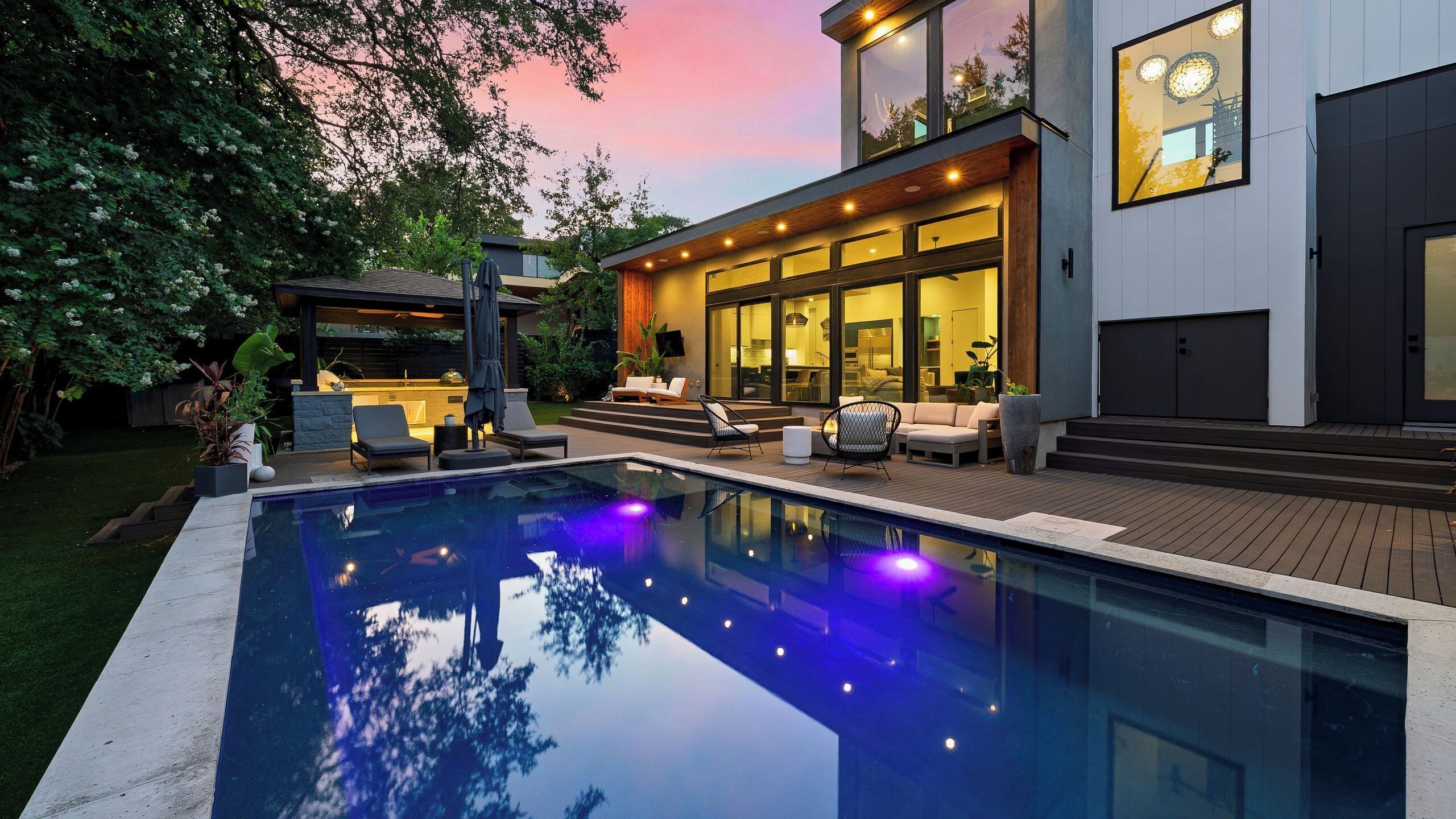 Une maison moderne dotée d’une piscine, d’un espace salon extérieur et d’une grande porte vitrée donnant sur l’intérieur.