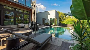 A modern outdoor pool area with lounge chairs, a covered seating area, and a view of the surrounding greenery.