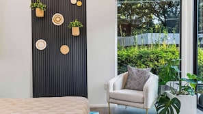 A modern interior with a bed, a chair, a wall-mounted plant arrangement, and a view of greenery outside.