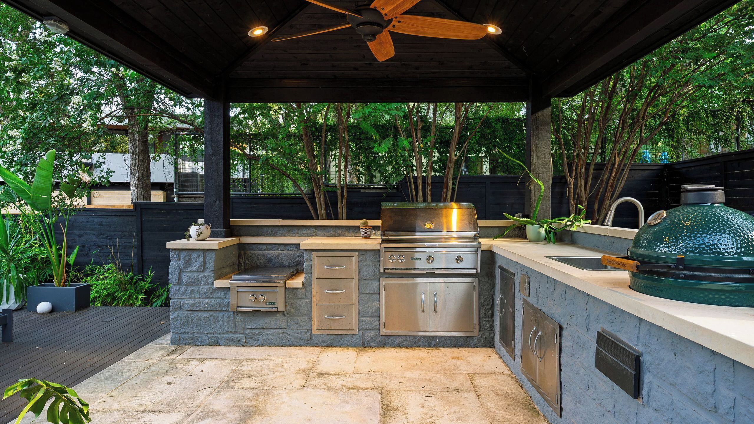 An outdoor kitchen with a grill, a built-in oven, and a ceiling fan.