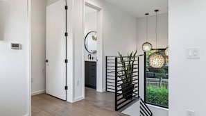 Un interior moderno con un pasillo que conduce a un baño, una escalera y vistas por una ventana.