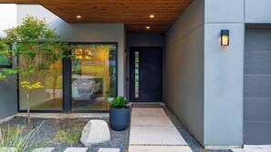 A modern exterior with a glass door entrance, a small tree, a potted plant, and a concrete pathway leading to a door.