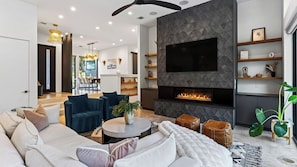 Una sala de estar moderna con chimenea, un televisor de pantalla plana grande y un comedor con luz natural.