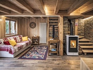 Ein gemütliches Blockhaus-Interieur mit Holzbalkendecke, Steinwand, Kamin, einer Couch und einer Uhr.