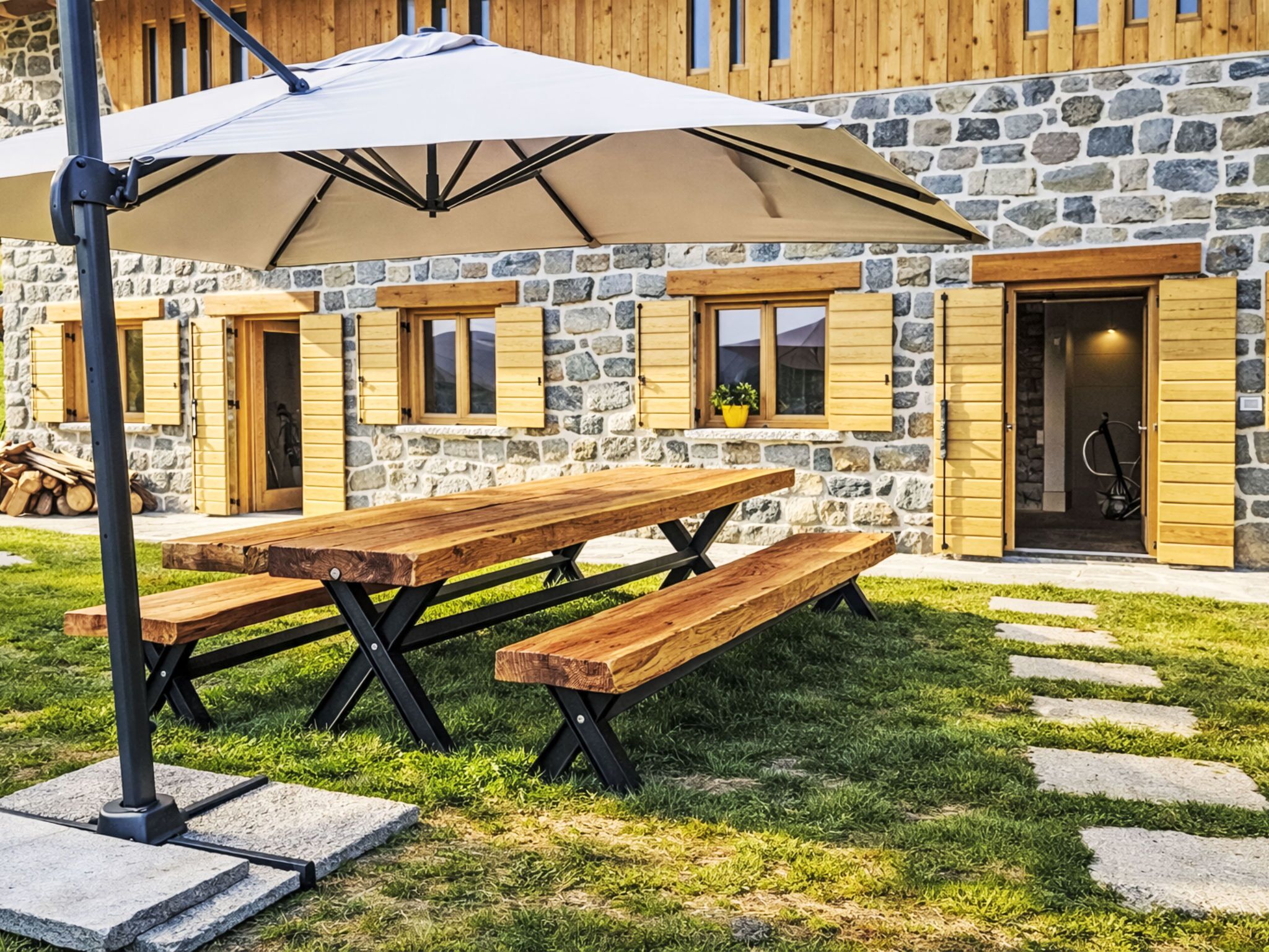 Un bâtiment en pierre avec des volets en bois, une table de pique-nique et un parasol.