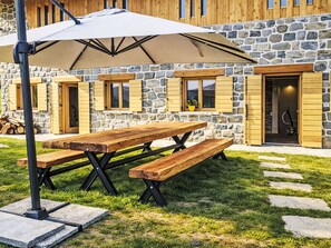 Un bâtiment en pierre avec des volets en bois, une table de pique-nique et un parasol.
