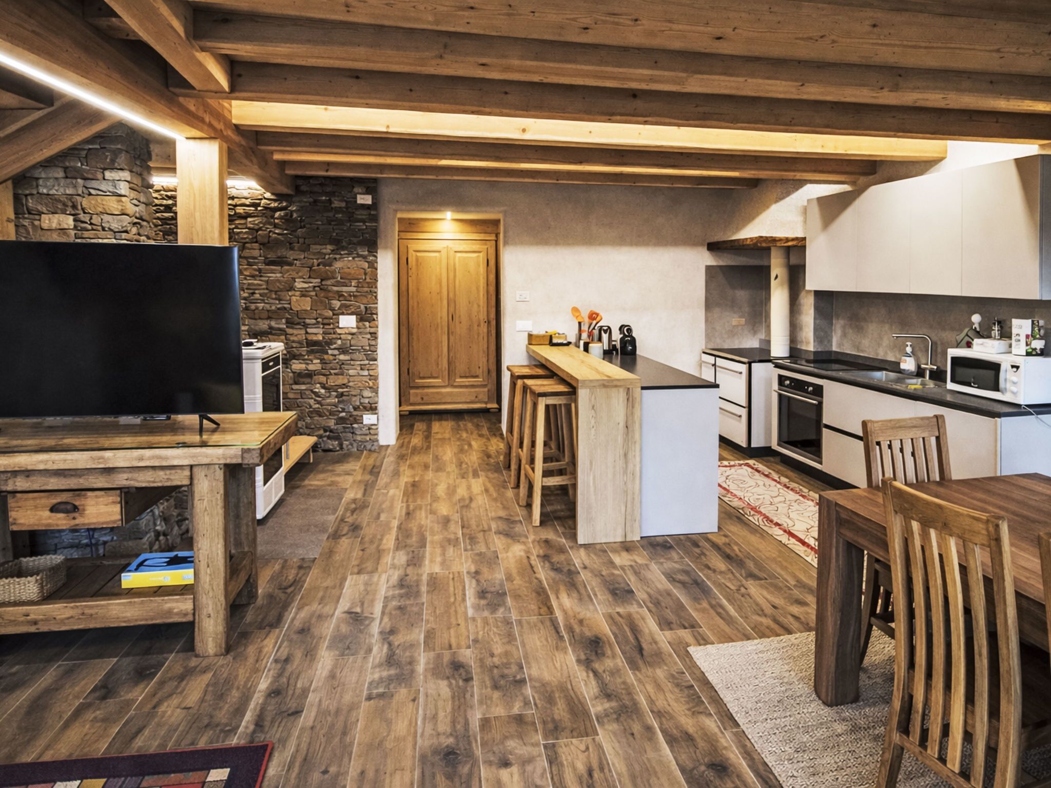 Une cuisine moderne avec un plancher en bois, un mur en pierre et un téléviseur encastré.