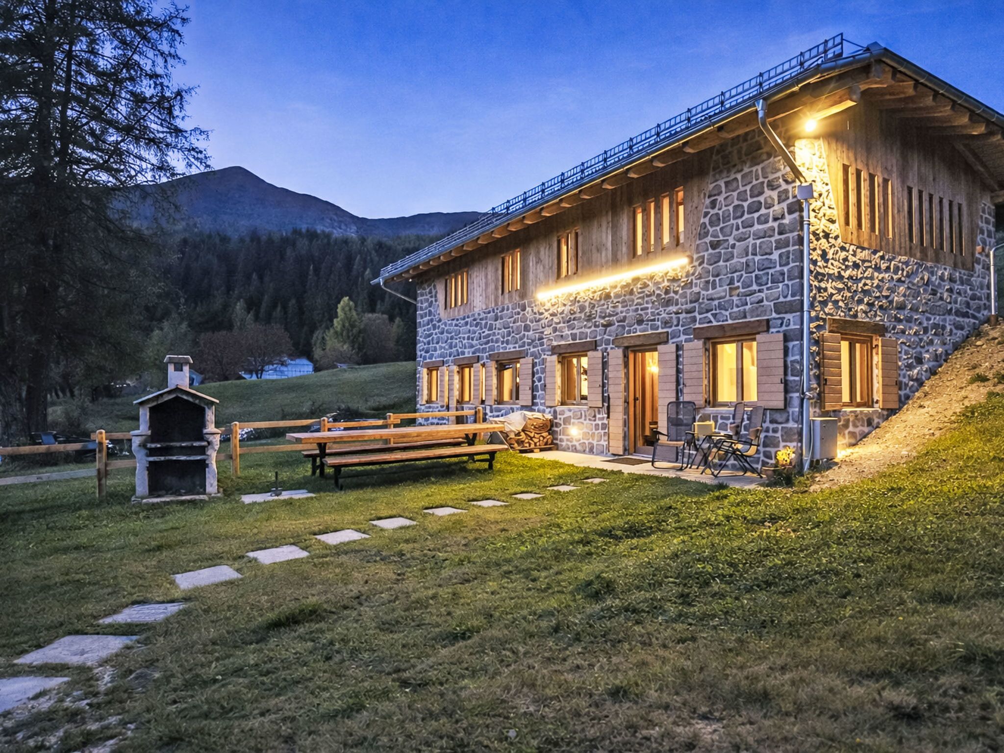 Un bâtiment en pierre doté d’une terrasse en bois, d’un barbecue et surplombant un paysage montagneux.