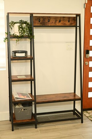 A tall, narrow metal shelf unit with multiple shelves and hooks, a basket, and a plant.