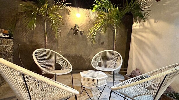 Un'area relax con sedie in vimini e un tavolino, circondata da un muro in pietra e piante di palma.