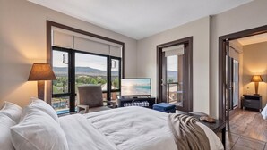 Quarto de hotel com cama, uma cadeira, televisão e vista para o exterior.