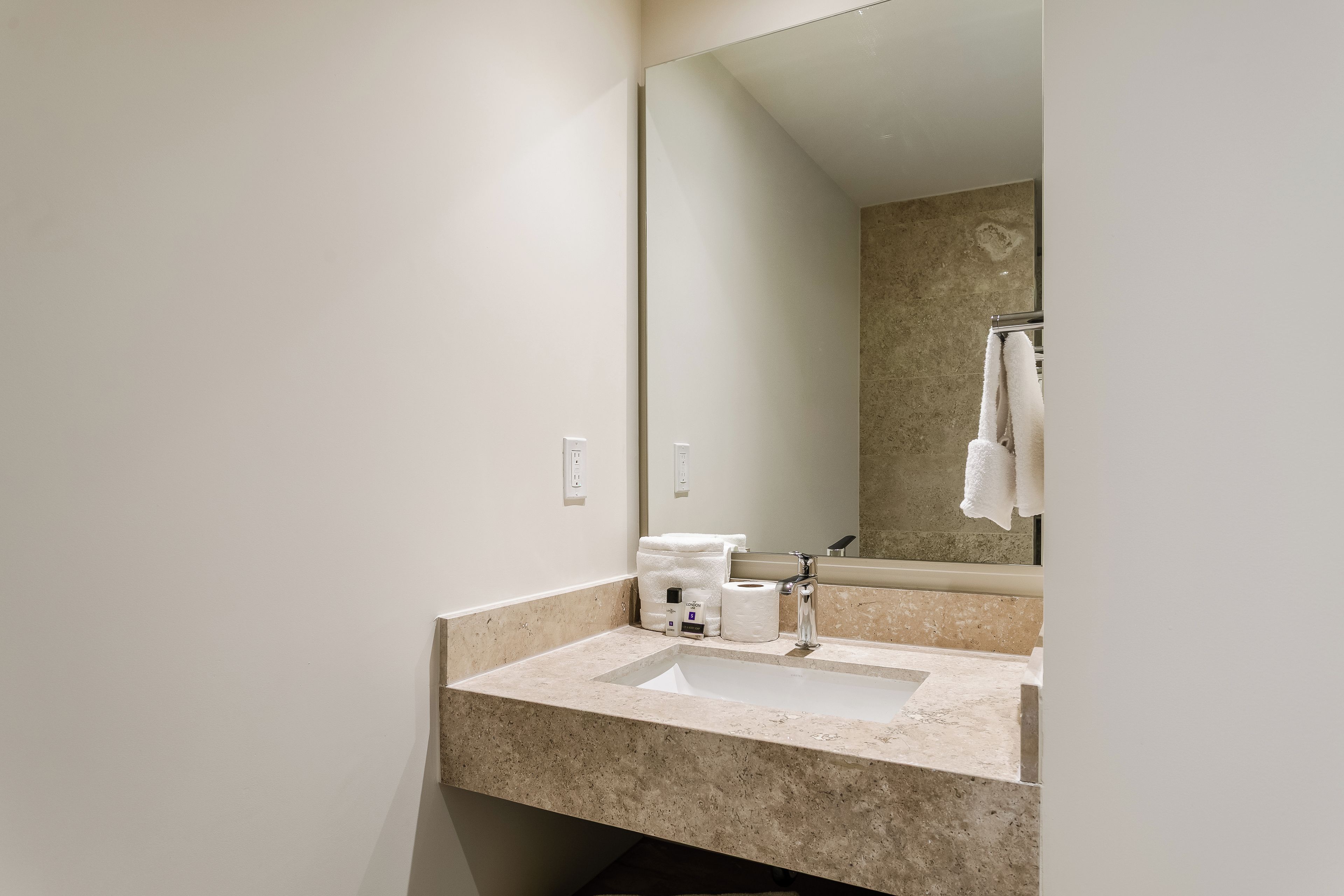 Une salle de bain équipée d’un lavabo, d’un miroir, d’un porte-serviettes et d’un plan de toilette en marbre.