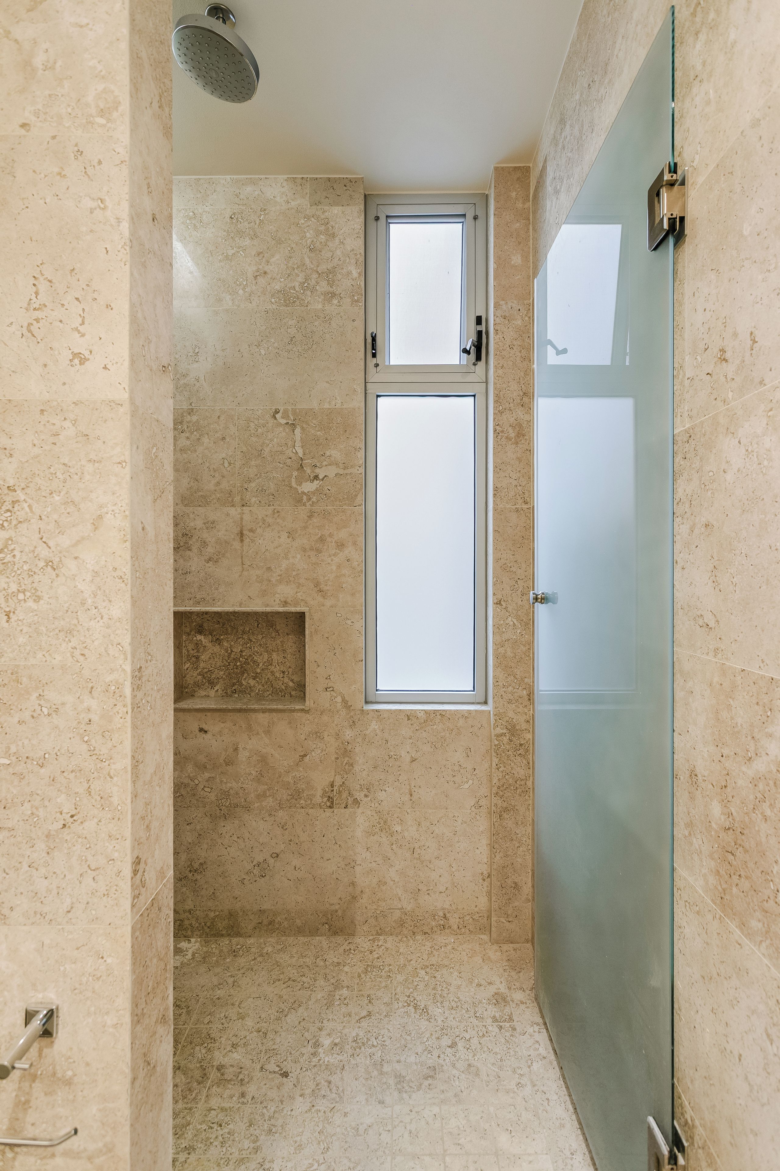 Un baño con cabina de ducha de vidrio, una ventana y una puerta.