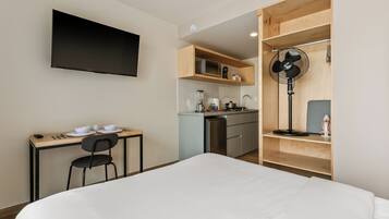 Habitación de hotel compacta con cama, kitchenette pequeña, mesa de comedor con sillas y televisor montado en la pared.