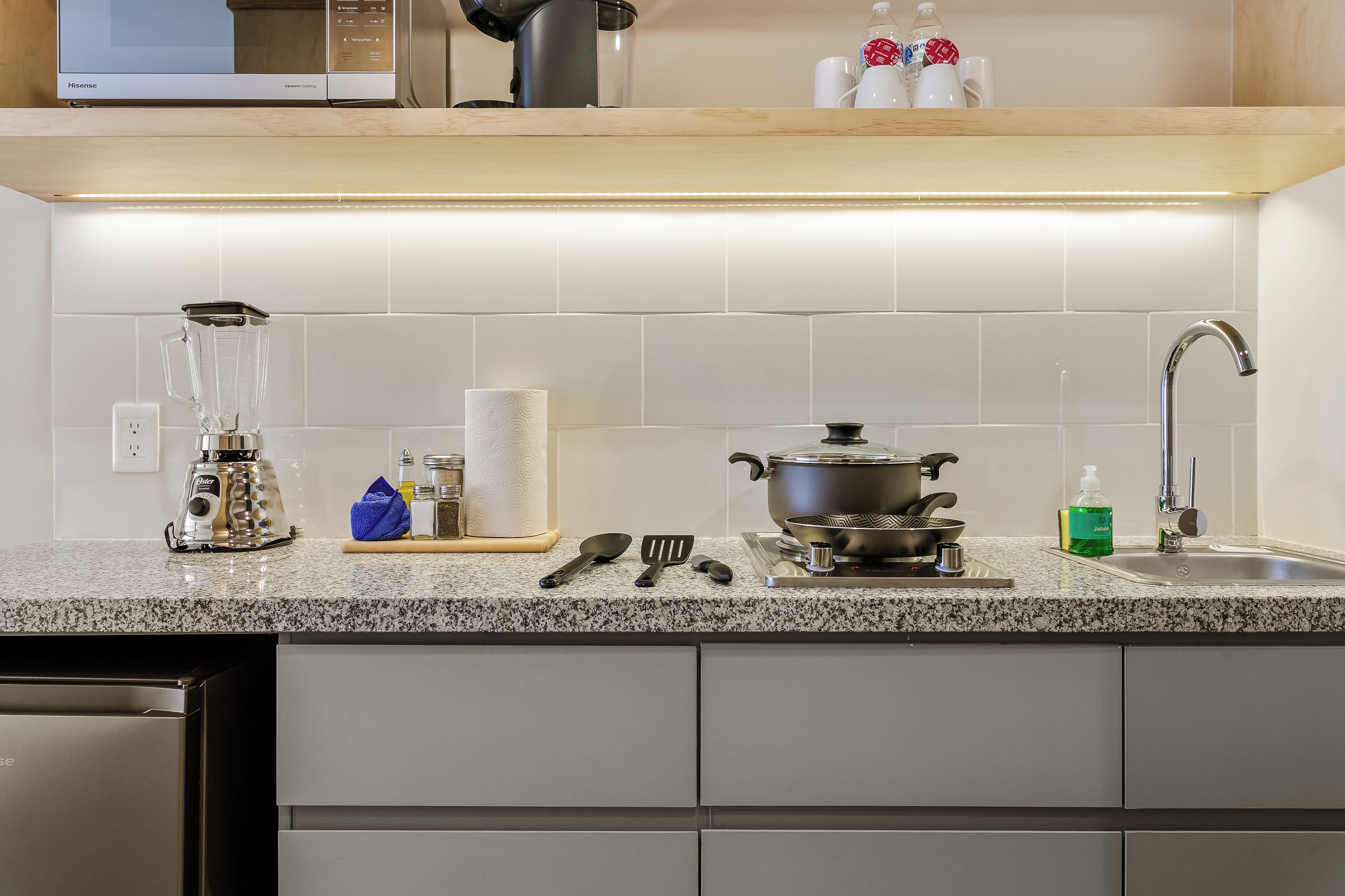 A kitchen with a granite countertop, a sink, a stove, and various kitchen utensils.