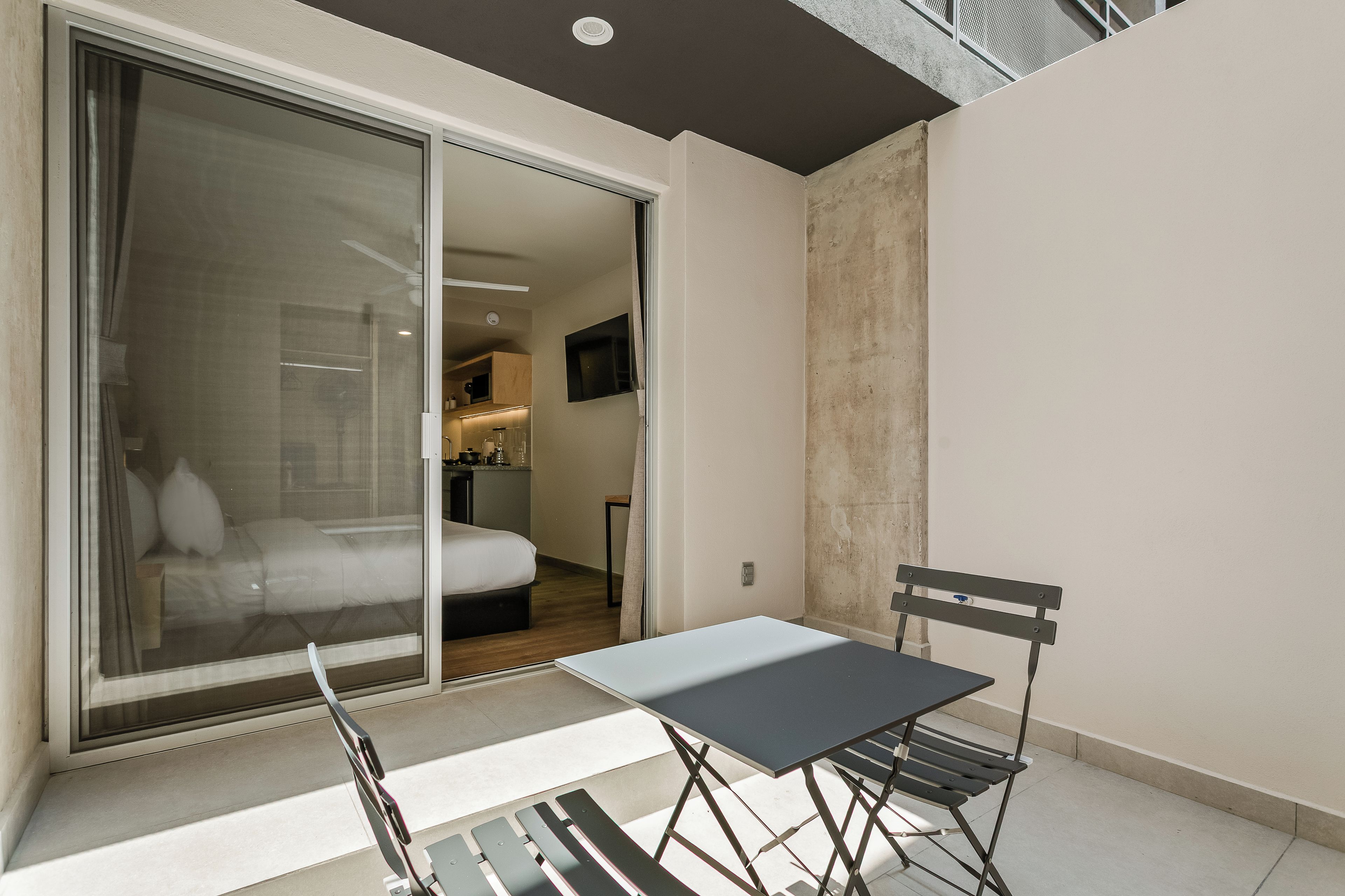 A modern hotel room with a balcony, a bed, a small table, and a chair.