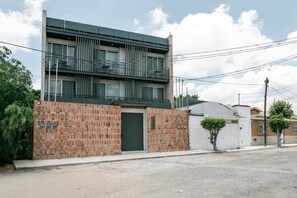 Un edificio moderno de dos pisos con fachada de ladrillo, entrada porticada y un pequeño árbol en la parte frontal.