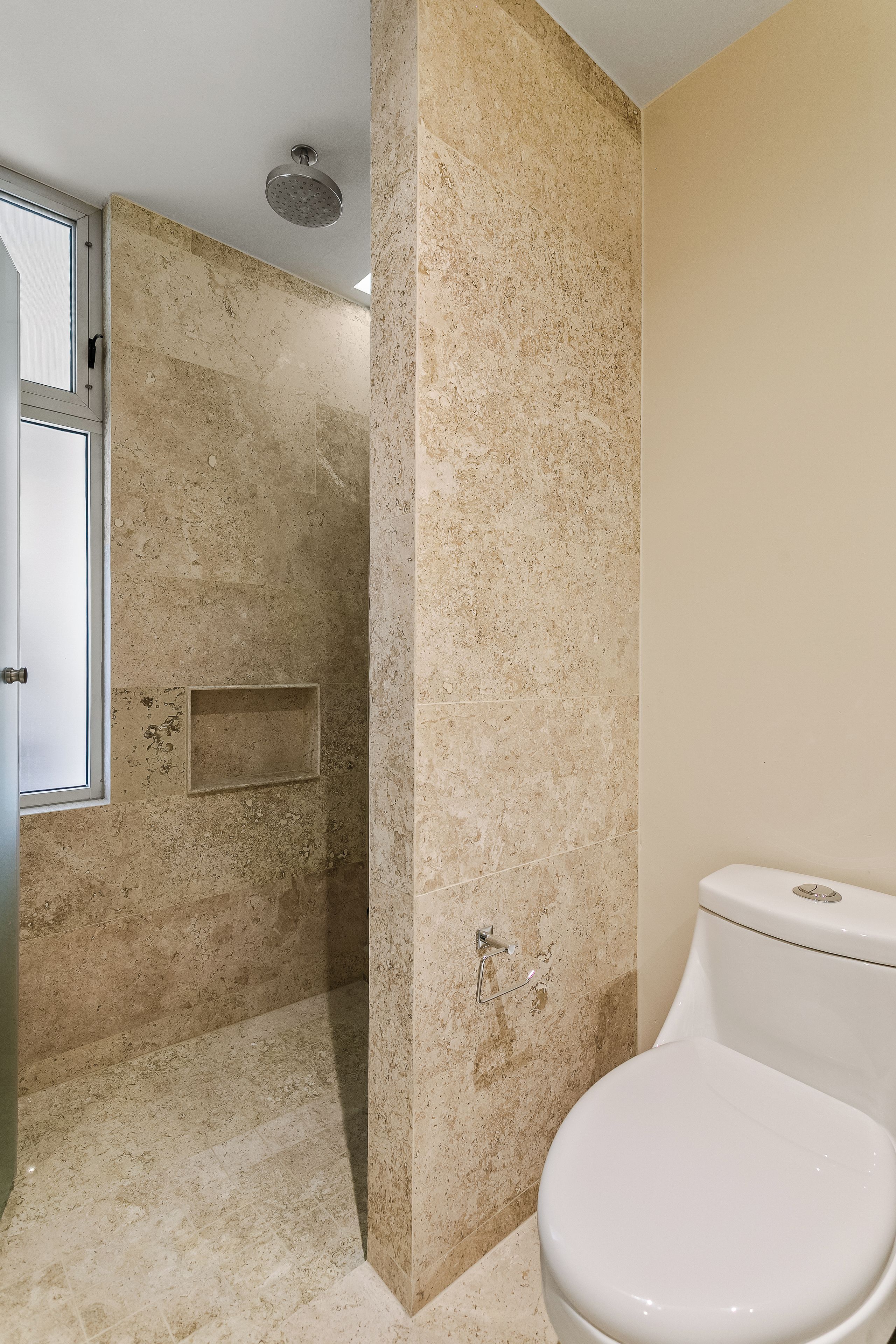 Un baño con ducha, inodoro y ventana.