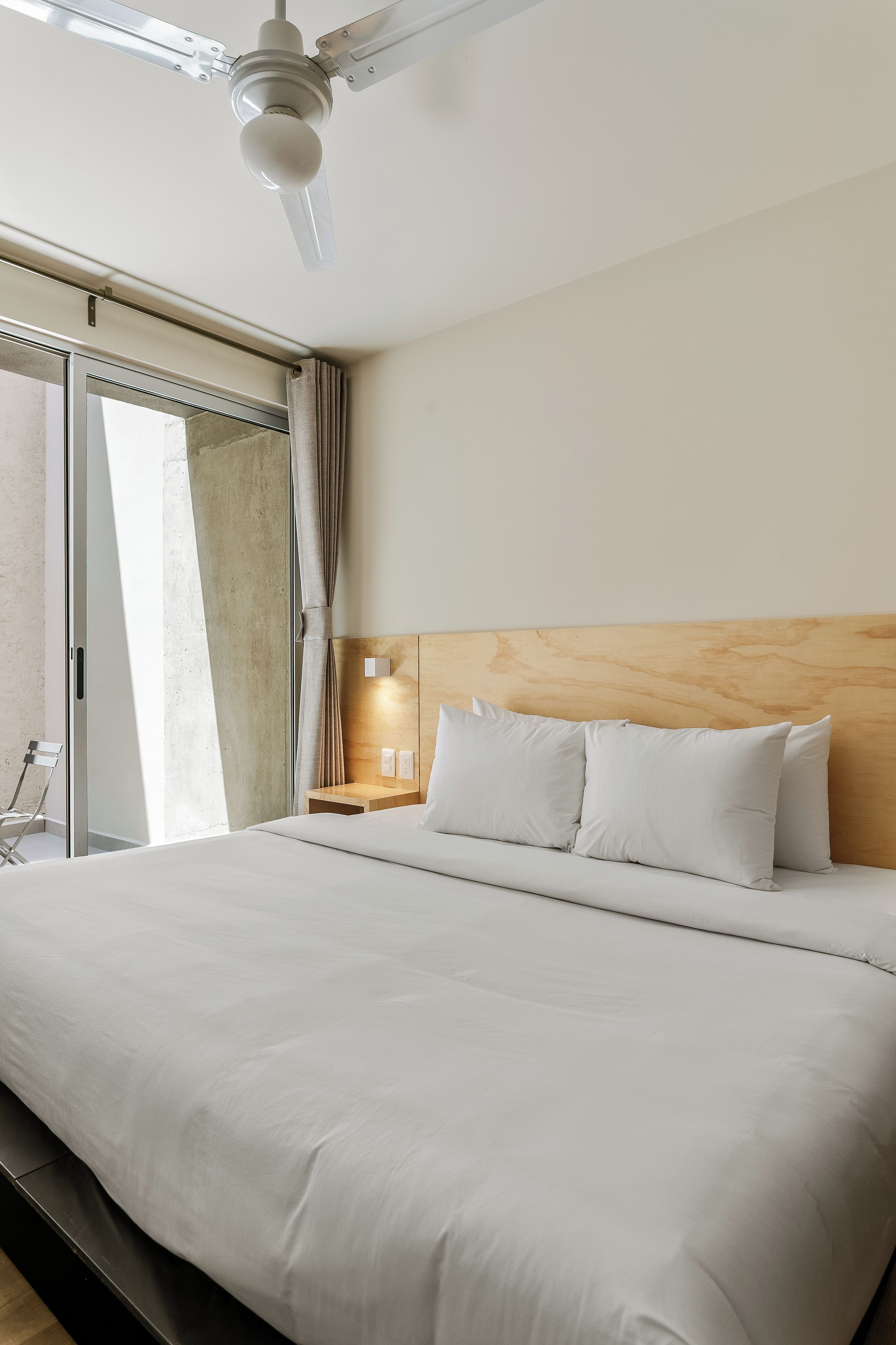 A hotel room with a large bed, a nightstand with a lamp, a wooden headboard, and a ceiling fan.