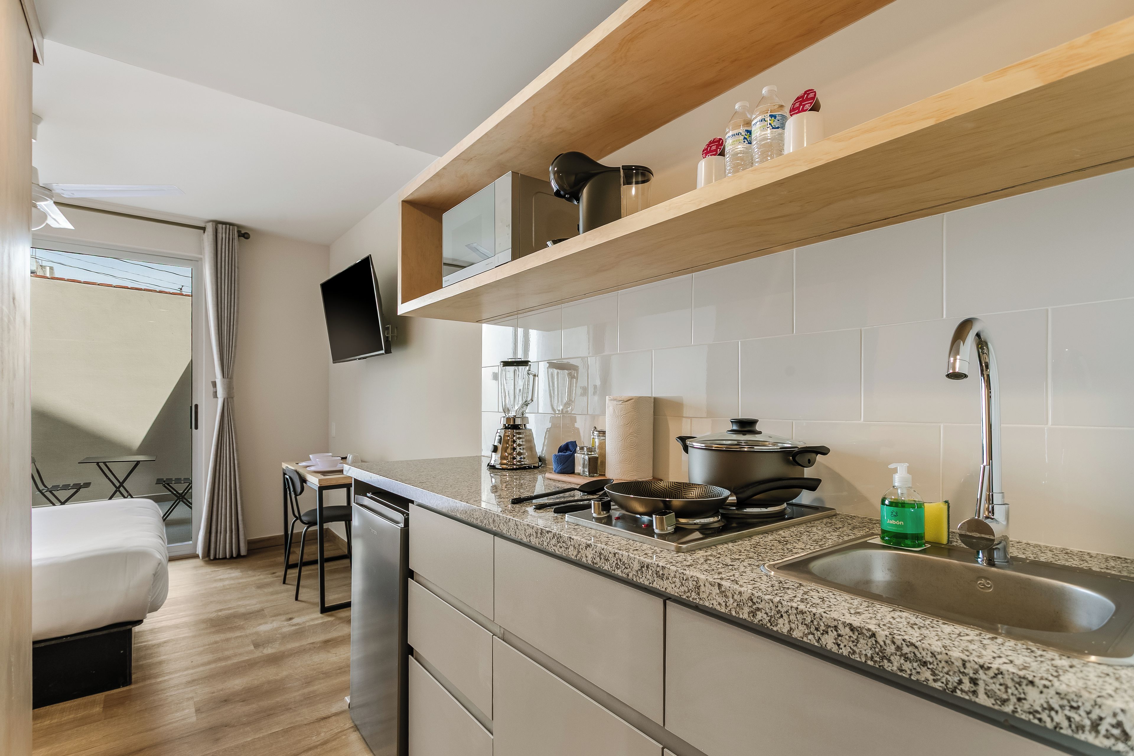 Una cocina moderna con encimera de granito, electrodomésticos de acero inoxidable y un estante de madera sobre el fregadero.