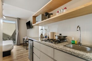 A modern kitchen with a granite countertop, stainless steel appliances, and a wooden shelf above the sink.