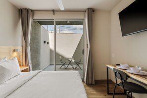 A hotel room with a bed, a desk with a chair, a dining table with plates and cutlery, and a TV on the wall.