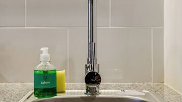 Un évier de cuisine avec un robinet, une bouteille de savon liquide vert et une éponge jaune.