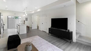 Uma sala de estar moderna com televisão de tela plana, uma cozinha com ilha central e uma escada que leva a um andar superior.