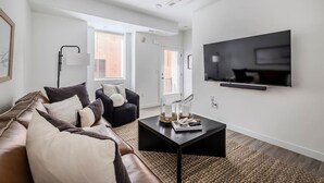 Een moderne woonkamer met een leren bank, een zwarte fauteuil, een salontafel en een wandgemonteerde televisie.