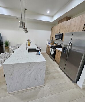 A modern kitchen with a marble island, stainless steel appliances, and wooden cabinets. - Modern 4BR New Home - Minutes to NRG, Med. Ctr, Downtown & UH (Houston)